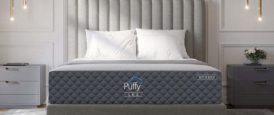 Puffy Lux mattress laying on a fabric decorated platform bedframe with luxurious pillows and high end lighting and side tables.