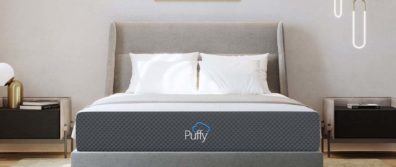 The Puffy Original mattress laying on a fabric platform bedframe with luxurious pillows and high end lighting and side tables.