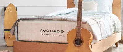 The Avocado ECO Organic Latex hybrid Mattress with a guitar in front. The mattress is on a wooden bedframe in a bedroom with a skateboard in the background.