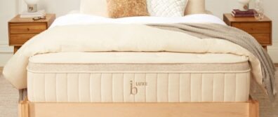Birch Luxe Natural Latex Mattress by Helix is resting on a natural wood bedframe in a master bedroom with end tables, pillows and sheets.